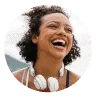 Smiling woman with curly hair and white headphones around her neck, set against a circular coral background. Represents joy, energy, and the supportive Noom community.